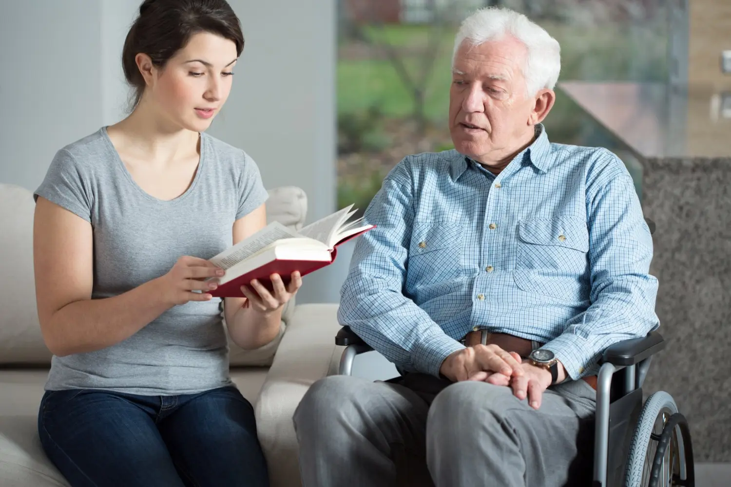 Eine junge Frau liest ein Buch, während ein alter Mann vom Lebensabend Pflegeleicht zuhört